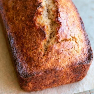 Loaf of easy homemade banana bread with ripe bananas and nuts on a cutting board.