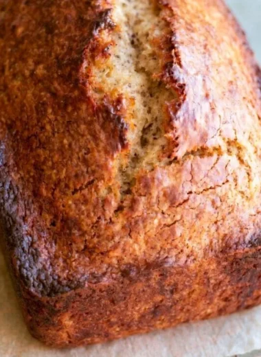 Loaf of easy homemade banana bread with ripe bananas and nuts on a cutting board.