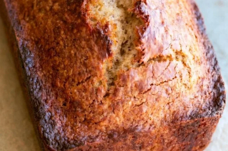 Loaf of easy homemade banana bread with ripe bananas and nuts on a cutting board.
