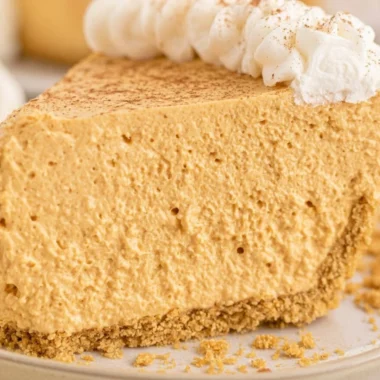 Fluffy marshmallow pumpkin pie slice on a plate, decorated with whipped cream.