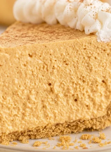 Fluffy marshmallow pumpkin pie slice on a plate, decorated with whipped cream.