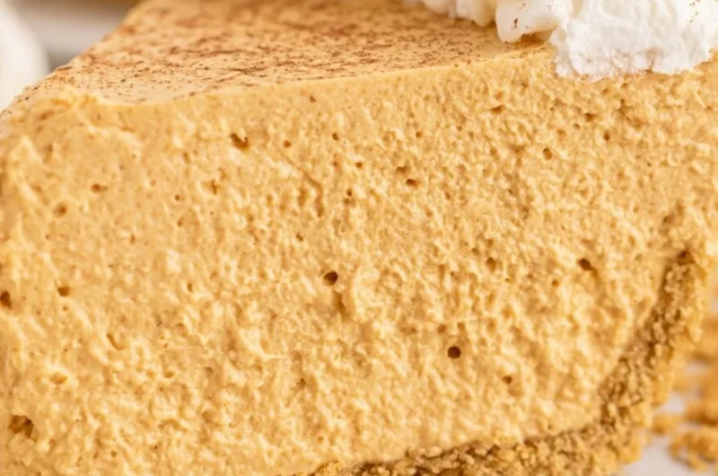 Fluffy marshmallow pumpkin pie slice on a plate, decorated with whipped cream.