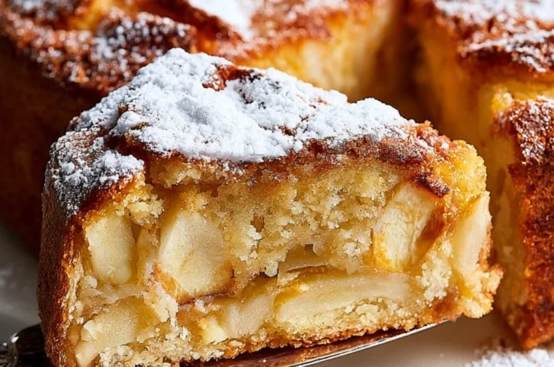 Slice of French Apple Cake with fresh apples and a dusting of powdered sugar