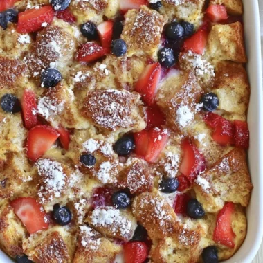 Delicious French Toast Casserole baked in a dish, topped with syrup and berries.