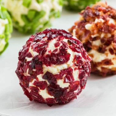 A platter of mini cheeseball bites topped with herbs and spices.
