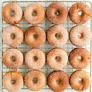 Freshly baked pumpkin spice donuts with icing and spices on a rustic table.