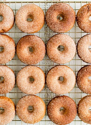 Freshly baked pumpkin spice donuts with icing and spices on a rustic table.