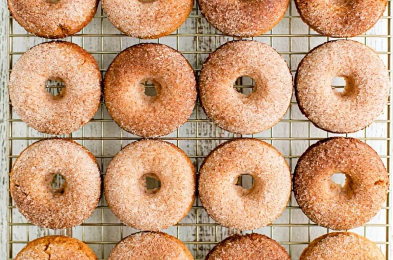 Freshly baked pumpkin spice donuts with icing and spices on a rustic table.