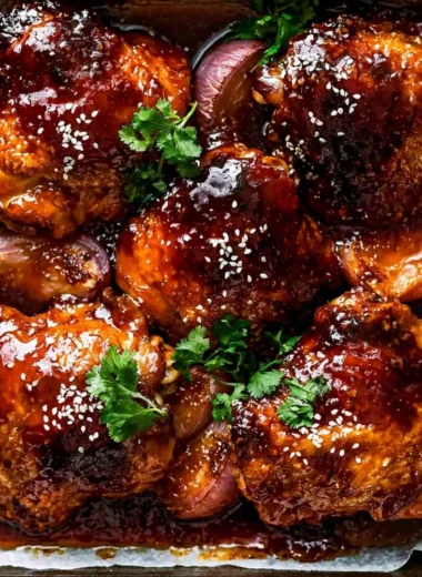 Baked sticky honey soy chicken on a plate garnished with sesame seeds and green onions.