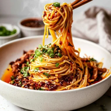 A plate of spicy Szechuan Noodles garnished with scallions and peanuts.