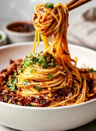 A plate of spicy Szechuan Noodles garnished with scallions and peanuts.