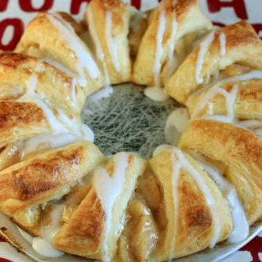 Freshly baked Apple Crescent Ring topped with sugar glaze on a white plate.