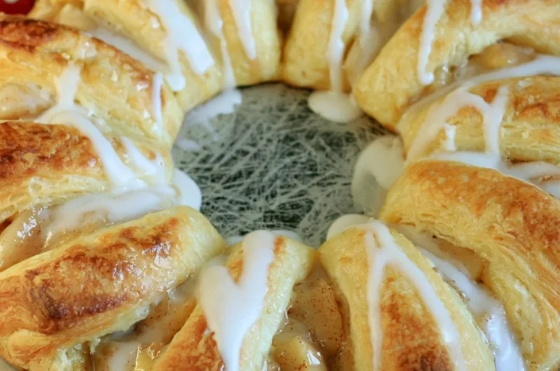 Freshly baked Apple Crescent Ring topped with sugar glaze on a white plate.