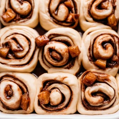 Freshly baked apple pie cinnamon rolls with a drizzle of icing on top