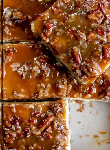 Pecan pie cheesecake bars topped with pecans and caramel drizzle